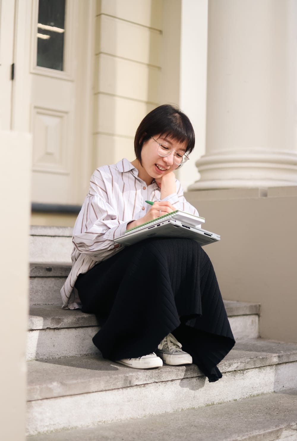 Woman writing notes on steps with laptop post image