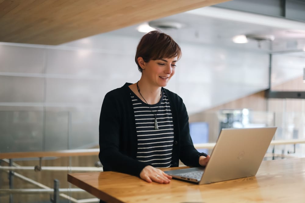 Woman smiling while working on laptop at a desk post image