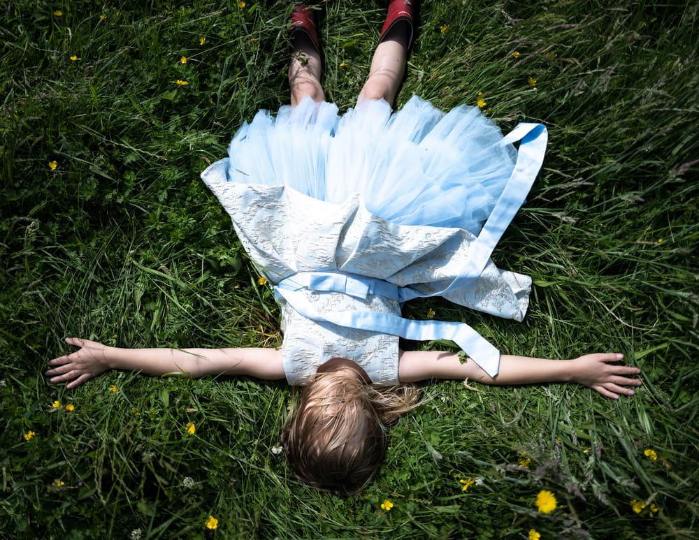 Child in a blue dress lying in the grass post image