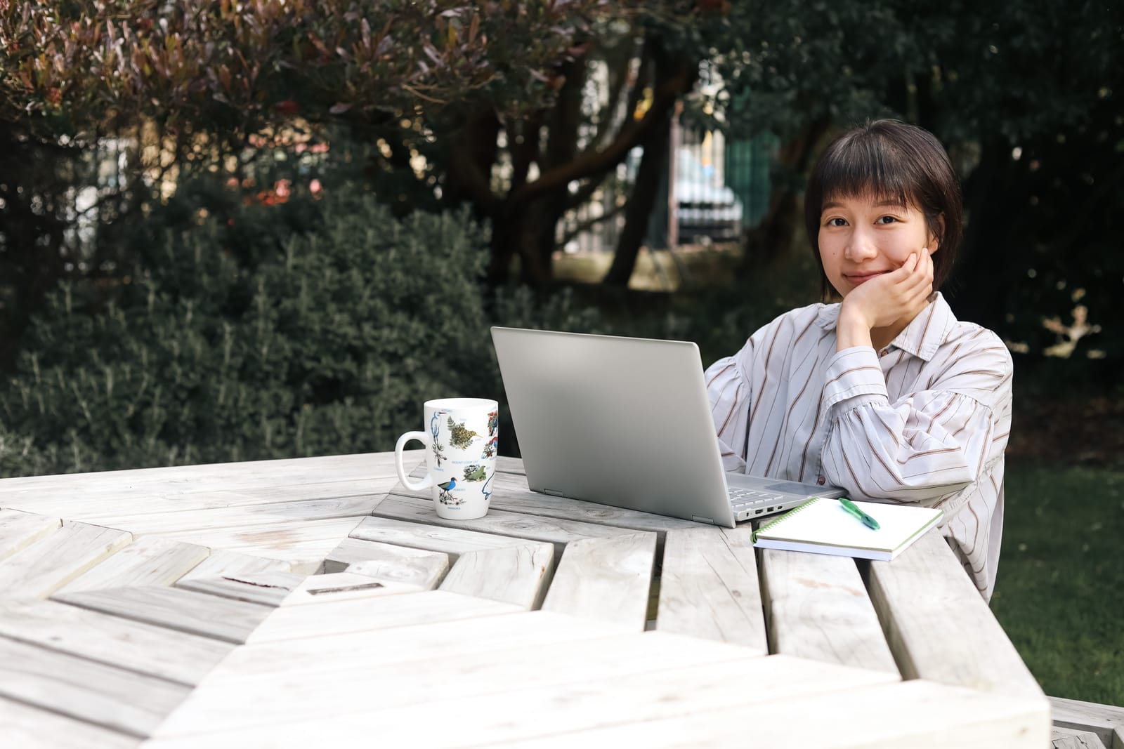 Woman working outdoors with laptop and coffee mug